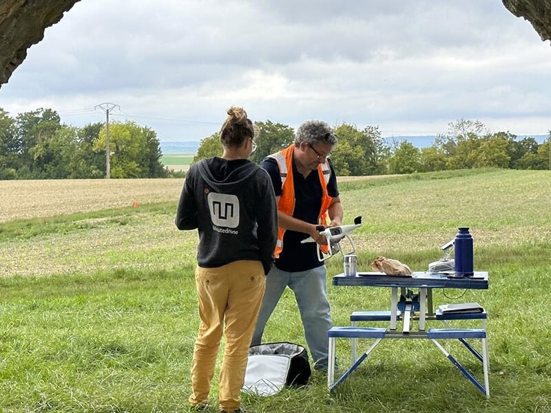 Un télépilote professionnel portant un chasuble orange prépare un drone lors d'un baptême de pilotage de drone