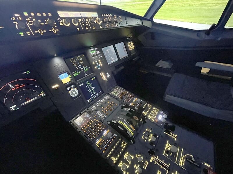 Gros plan sur les instruments du tableau de bord d’un cockpit simulé, affichant cadrans, écrans de navigation et commandes éclairées.