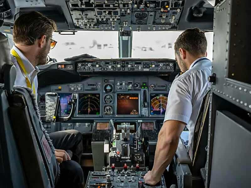 Deux pilotes en uniforme dans le cockpit d'un avion, entourés de nombreux instruments et écrans de contrôle.