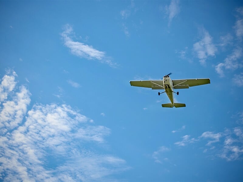 Un Cessna 172 vole à basse altitude dans un ciel bleu avec quelques nuages