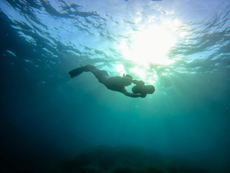Plongeur solitaire avec palmes et tuba nage sous l'eau, éclairé par un soleil éclatant à travers la surface marine.