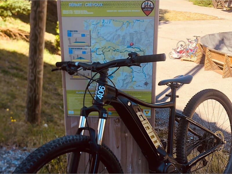 Un VTT électrique appuyé sur le panneaux indiquant les itinéraires à vélo dans les environs du Crévoux
