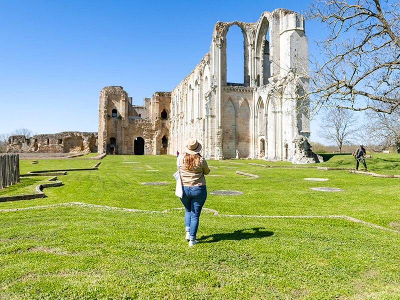 Une femme portant un jean bleu regarde les ruines de l'abbaye de Maillezais