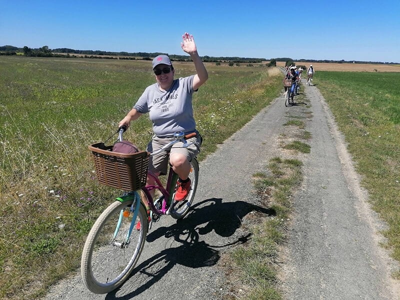Une femme à vélo salue le photographe sur une piste cyclable qui traverse le marais Poitevin