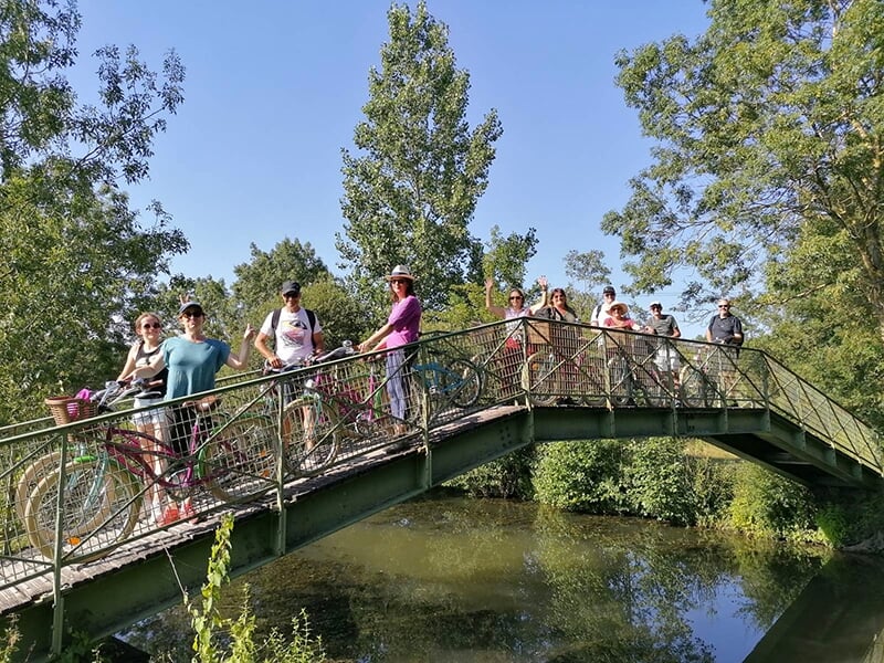 Un groupe de cylistes à l'arrêt sur une passerelle qui enjambent un canal dans le marais Poitevin