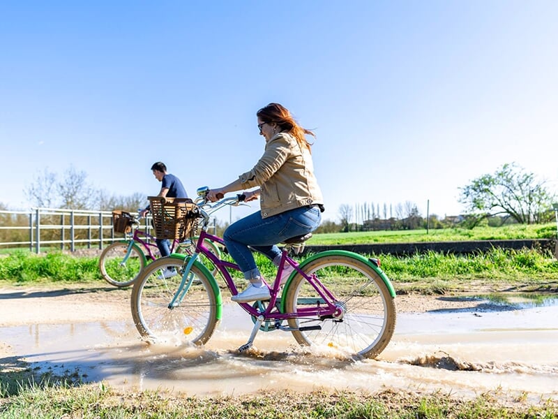 Une femme à vélo roule dans une flaque d'eau sur une piste cyclable qui borde un canal.