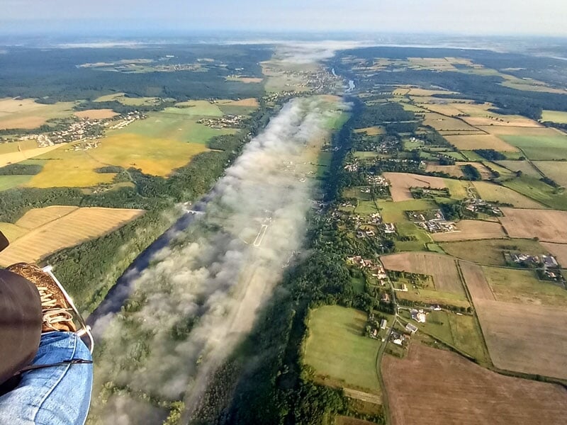 Vue aérienne d'une bande de brouillard s'étendant à travers un paysage de champs et de forêts