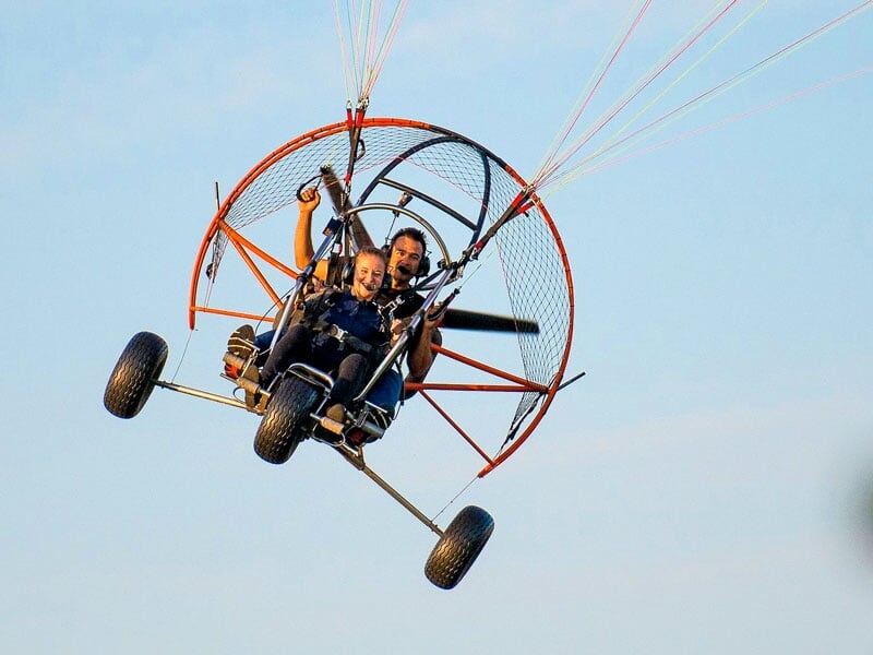 Un paramoteur en vol avec une passagère souriant