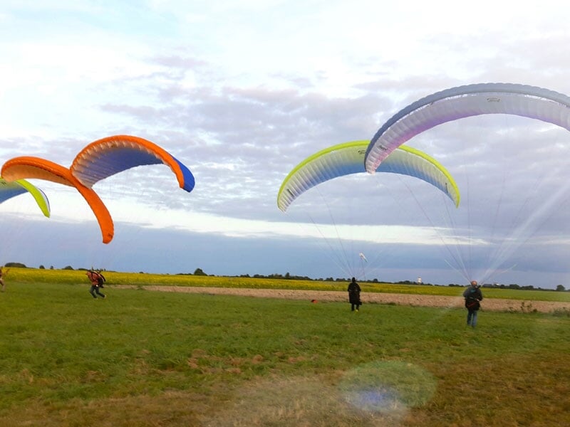 Plusieurs parapentes colorés se préparant pour le vol dans un champ