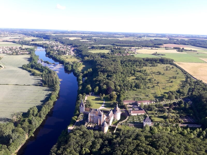Vue aérienne d'un château médiéval avec des douves, entouré par un paysage verdoyant
