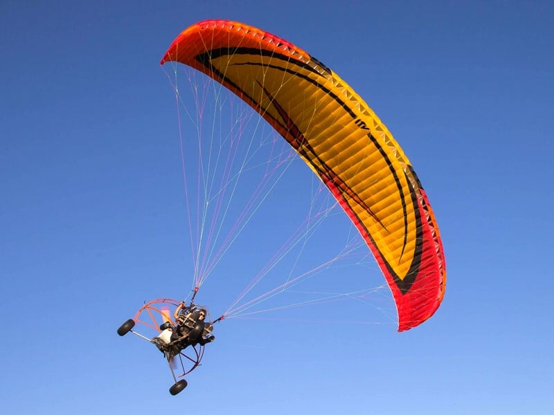 Un paramoteur avec une voile orange et jaune dans le ciel bleu