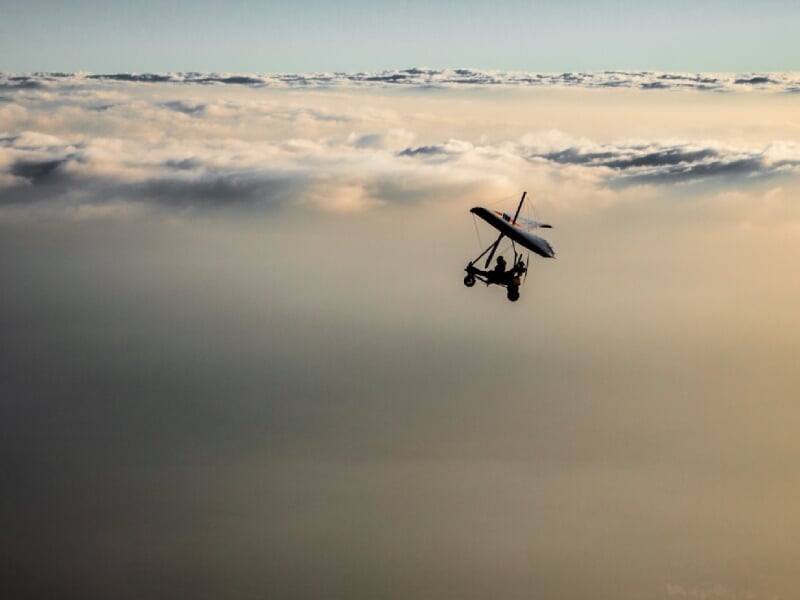 Deltaplane évoluant à haute altitude, au-dessus d'une couche dense de nuages blancs, avec un fond de ciel bleu clair, créant une impression de sérénité et d'isolement au-dessus du monde.