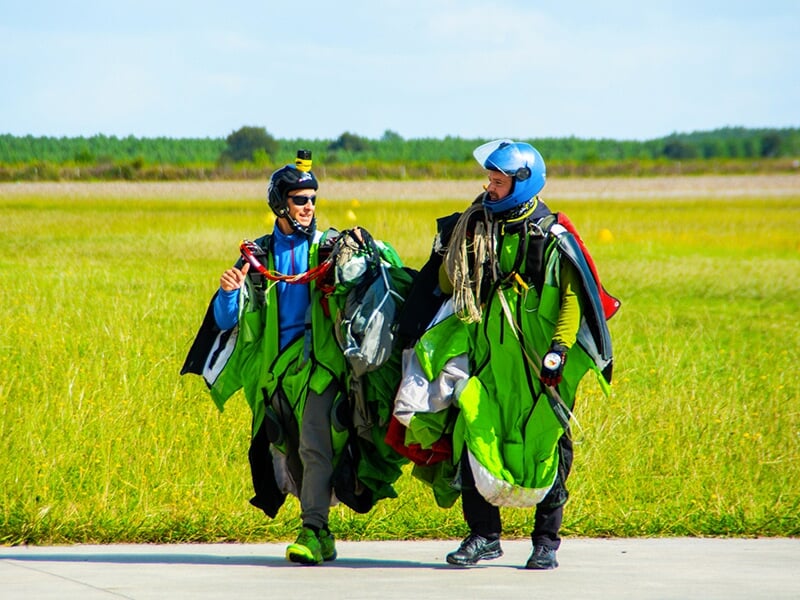 Deux parachutistes marchant côte à côte après leur saut, en combinaison verte et casque, portant leur équipement de parachutisme.