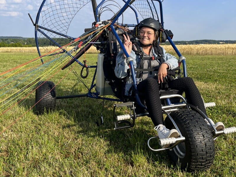 Une jeune dans le chariot d'un paramoteur fait le V de la victoire pendant son baptême de l'air en ULM