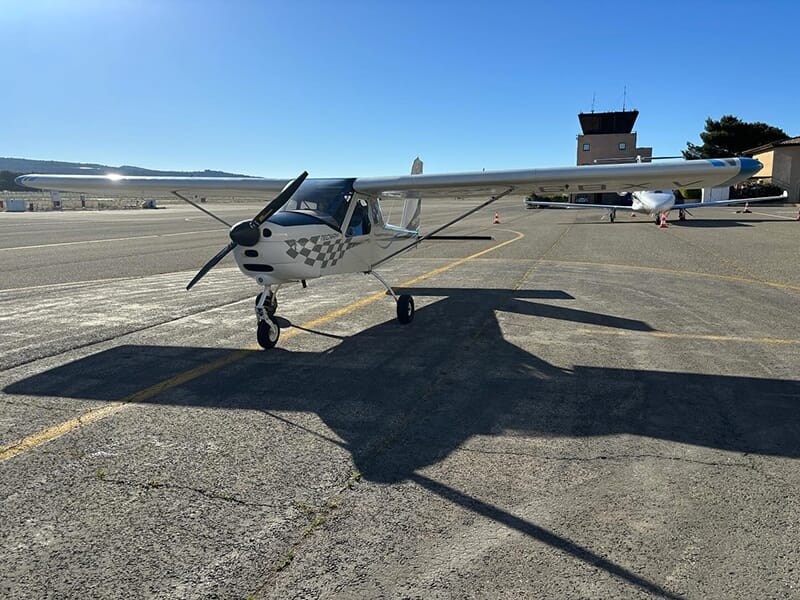 Un avion Tecnam P92 posé sur le tarmac d'un aérodrome avec la tour de contrôle en arrière-plan.