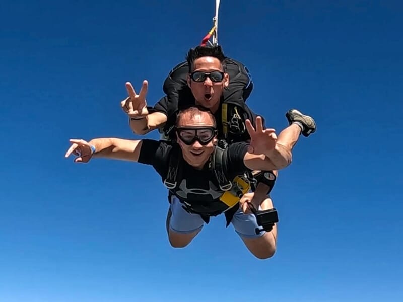 Deux hommes en chute libre en tandem lors d'un saut en parachute sous un ciel bleu clair sans nuages.