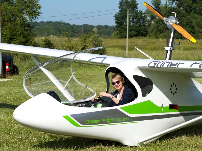 Femme souriante assise dans le cockpit d'un planeur blanc et vert marqué