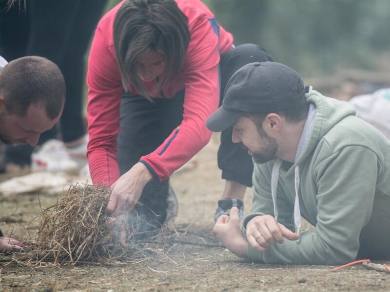 Trois personnes s'agenouillent au sol et tentent d'allumer un feu avec des brindilles.