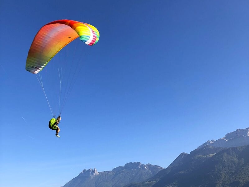 Un parapente vole au dessus des Alpes en plein été avec un ciel bleu en toile de fond