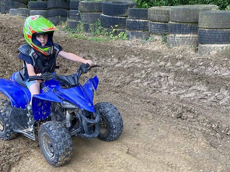 Un jeune de moins de 10 ans roule sur une piste de quad en terre avec des pneus en arrière-plan