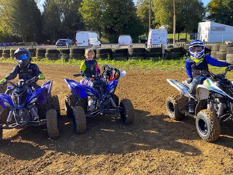 Trois enfants posent pour la photo sur des quad Yamaha lors d'un stage de pilotage sur un circuit de motocross