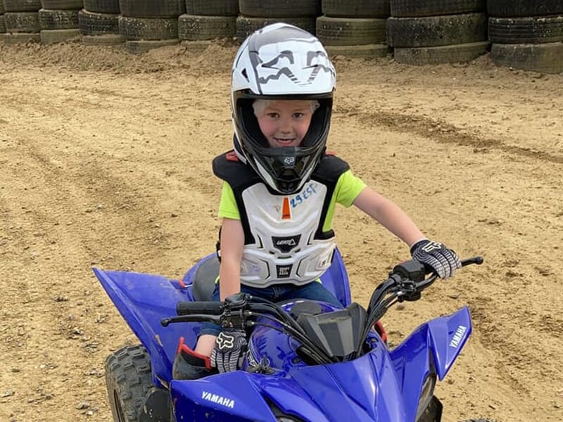 Un enfant casque sur la tête teste le pilotage de quad lors d'une stage sur un circuit en terre