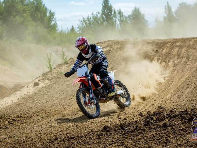 Un pilote de motocross négocie un virage sur une piste en terre avec des arbres en arrière-plan