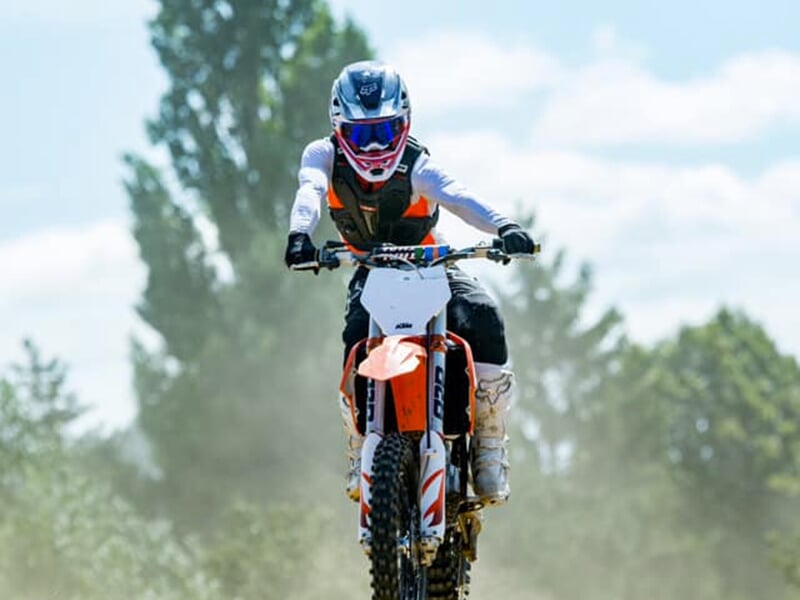 Un pilote de cross accélère sur une piste de cross avec des arbres en arrière plan
