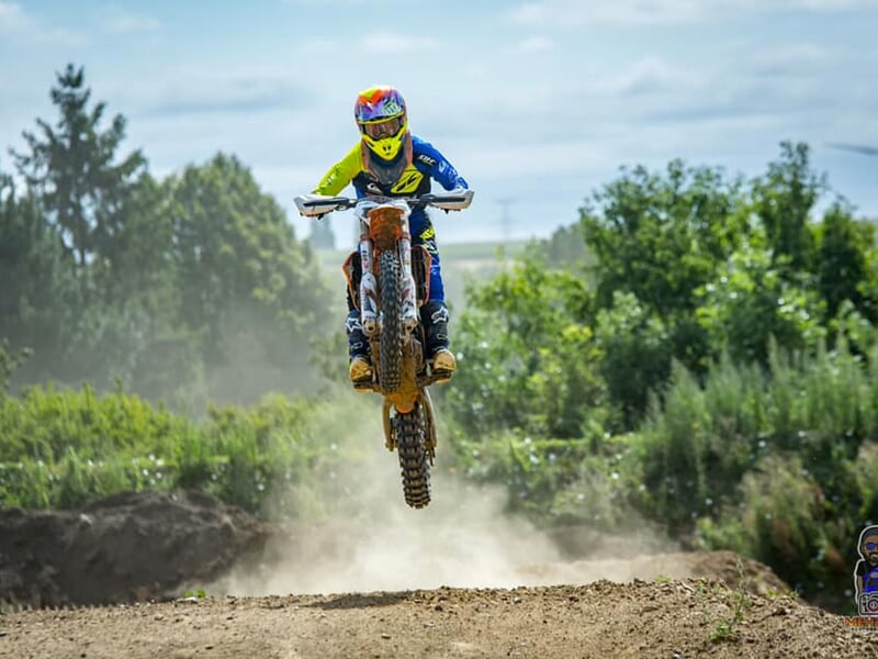 Un pilote de cross en suspension soulève un nuage de poussière sur une piste de motocross boisée