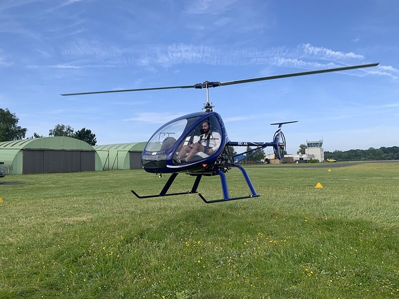 Un hélicoptère ULM fait un vol stationnaire au-dessus de la piste d'un aérodrome de province.