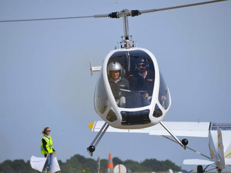 Un hélicoptère Dynali H3 décolle d'un aérodrome avec à son bord un pilote et un passager