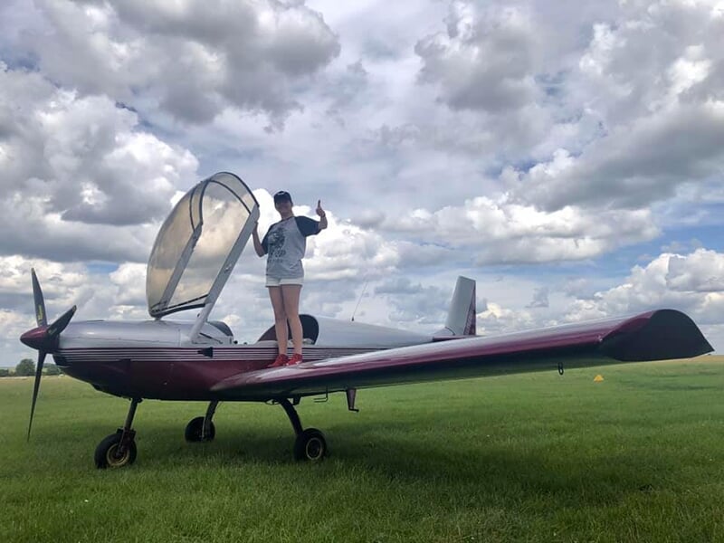 Une jeune femme debout sur l'aile d'un avion ULM pose avant son baptême de l'air à Amiens