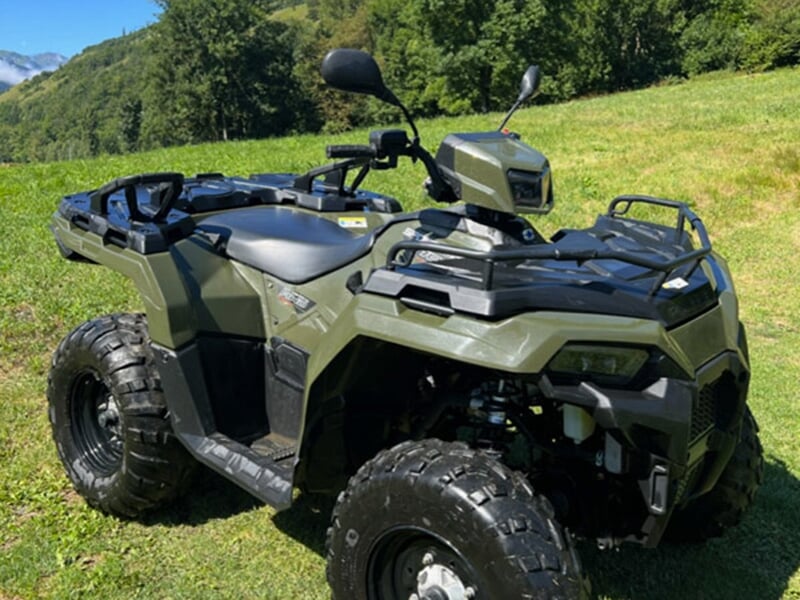 Un quad monoplace de couleur verte stationné dans un pré avec une forêt en arrière-plan