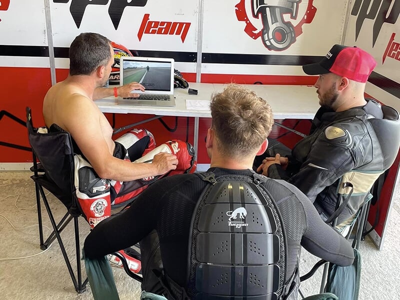Un coach de moto avec ses deux stagiaires font un débriefing vidéo d'une session de pilotage sur circuit
