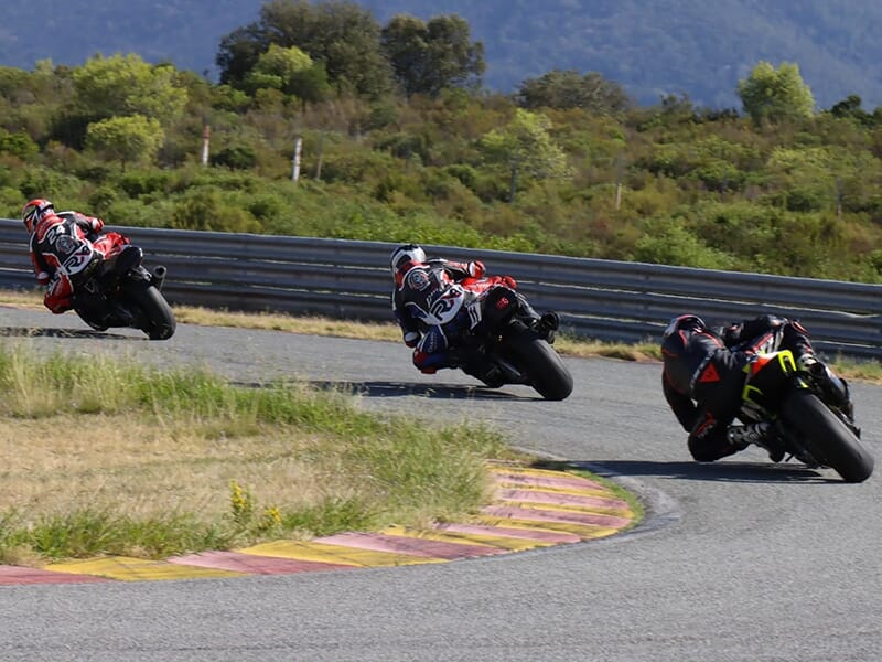 Trois motards en tenue de course prennent un virage serré sur un circuit au Driving Center du Castellet, sous un ciel clair.