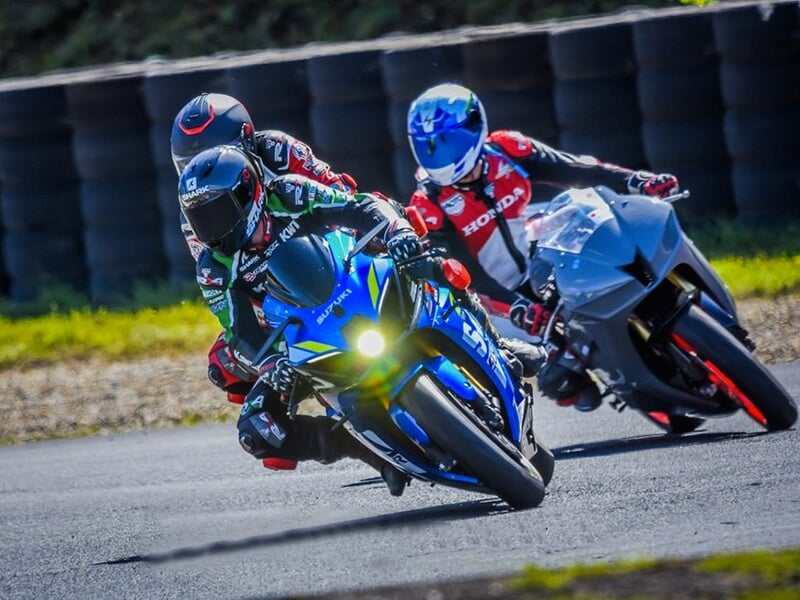 Un pilote et son passager sur la piste en asphalte d'un circuit de vitesse suivi par un autre pilote