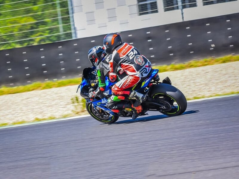 Deux motards en tenue de course sur une moto bleue prenant un virage sur une piste de circuit au Castellet.