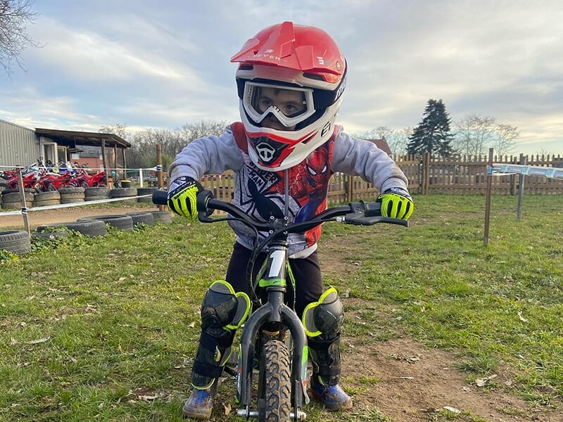 Un enfant équipé d'un casque, de gants et de genouillères découvre le motocross sur une draisienne électrique