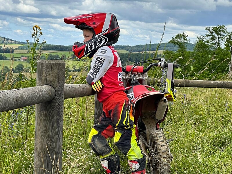 Un jeune pilote casque sur la tête regarde la piste appuyé sur la rambarde de sécurité d'un circuit en terre en Saône-et-Loire