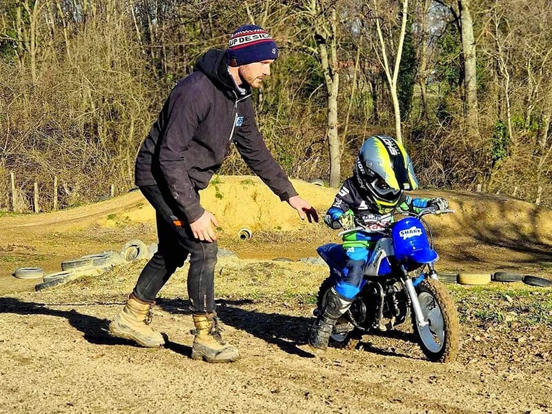 Un moniteur de moto apprend à un très jeune enfant à piloter une moto tout-terrain lors d'un stage d'initiation