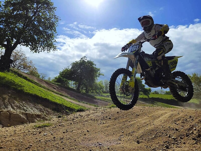 Un pilote de motocross saute une bosse sur une piste en terre entourée d'arbres en plein au milieu de la campagne