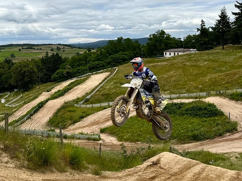 Un pilote de motocross effectue un saut sur une bosse sur une piste en terre en plein au milieu de la nature