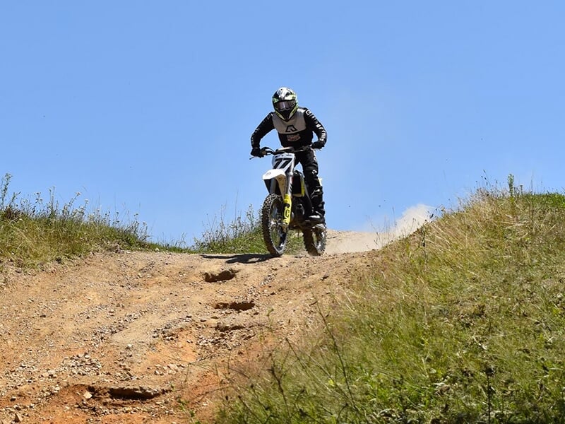 Un pilote de moto amorce une descente sur une piste en terre située en plein coeur de la nature