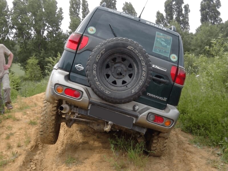Vue arrière d'un 4x4 en montée sur un terrain accidenté avec un homme debout à côté lors d'un stage 4x4.