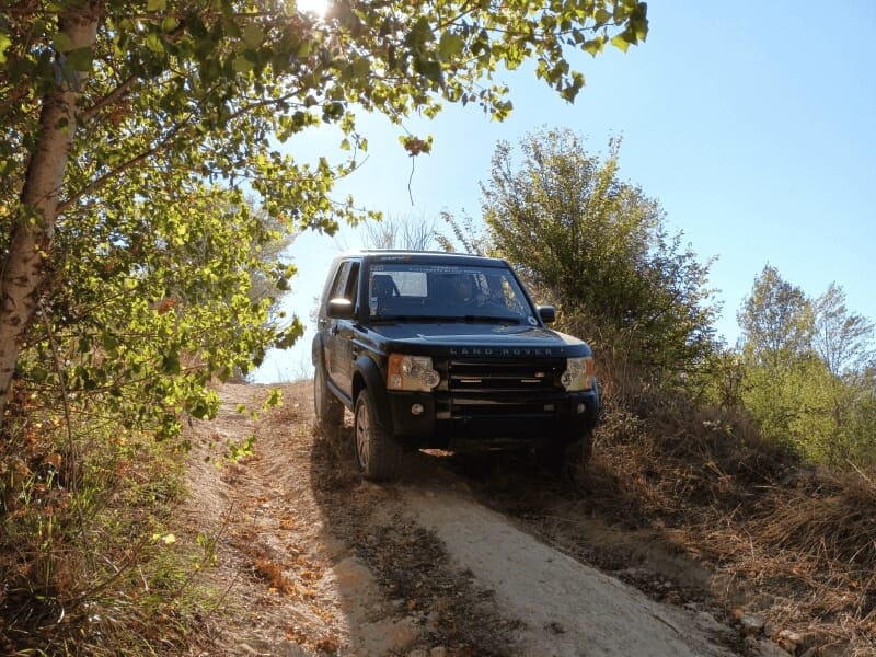Un Land Rover noir descend une pente en terre entourée d'arbres lors d'un stage 4x4.