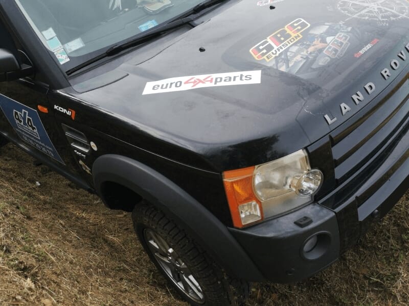 Vue partielle d'un Land Rover noir avec des autocollants sur le capot, lors d'un stage 4x4.