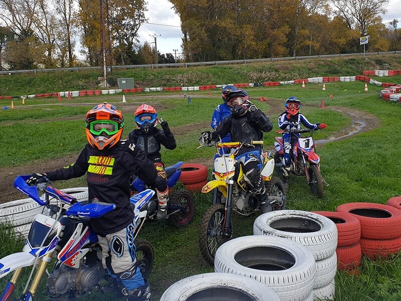 Groupe de jeunes pilotes de motocross en position de départ, prêts pour une course sur une piste extérieure, entourés de pneus de protection.
