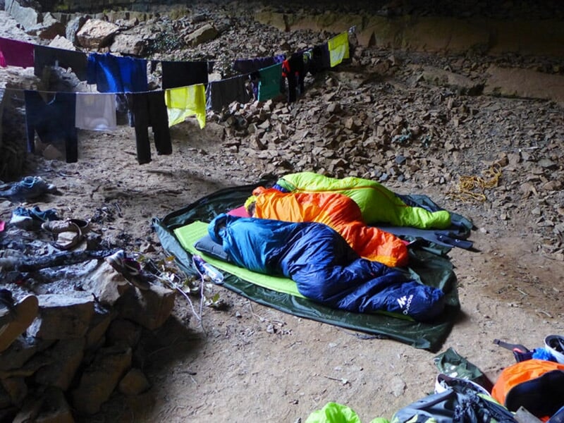 Un goupe d'aventuriers dort dans une grotte dans des sacs de couchage en plein coeur de la nature