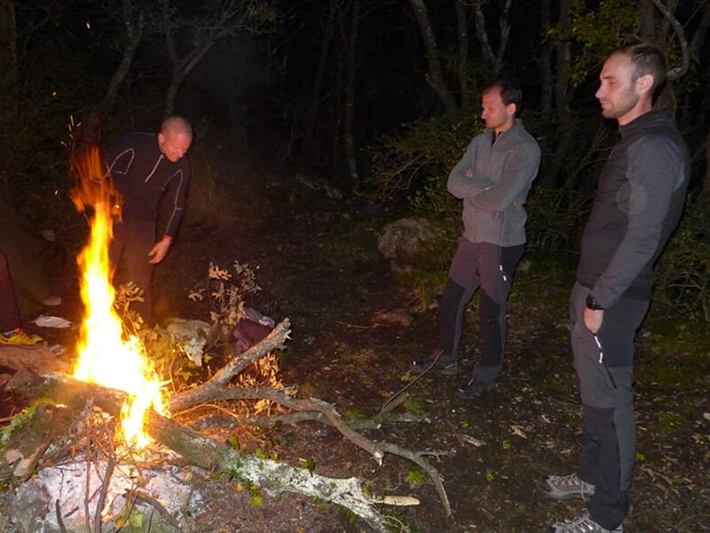 Des participants d'un stage de survie autour d'un feu après une journée d'efforts