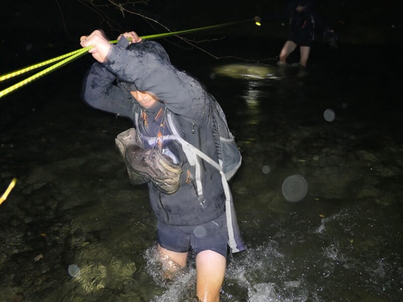 Un homme traverse une rivière à l'aide d'une corde dans la nuit lors d'un stage de survie